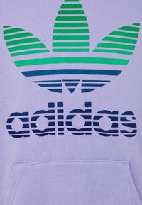 Paarse stof met groen en blauw gestreept Adidas trefoil-logo boven blauwe gestreepte "adidas"-tekst en een kangoeroezak.
