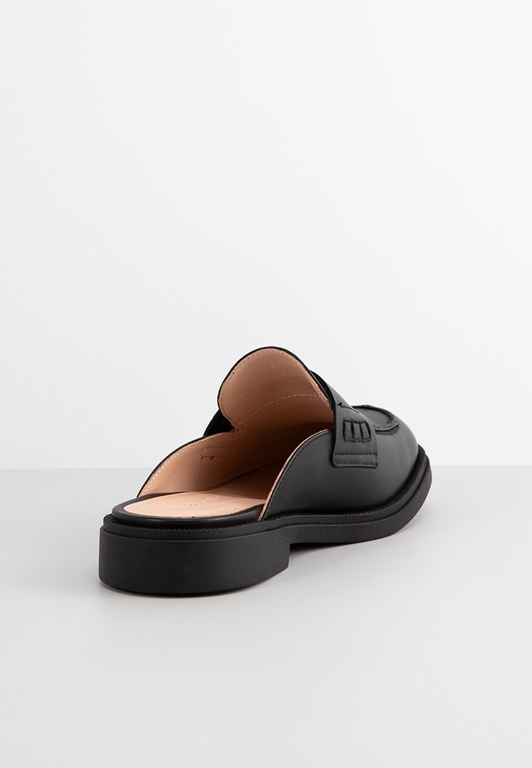 Schwarzer Leder Slipper mit glatter Oberfläche, abgerundetem Zeh und niedriger, strukturierter Gummisohle. Mit dekorativem Riemen über der Oberseite.