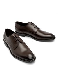 Zapatos de vestir de cuero marrón con un acabado suave, punta afilada y diseño de cuatro ojales con cordones. Presentan una silueta elegante y minimalista.