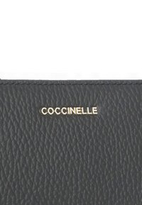 Czarny skórzany portfel o teksturowanej powierzchni z złotym logo "COCCINELLE". Zawiera widoczne przeszycia i gładkie wykończenie. Kompaktowy prostokątny kształt.