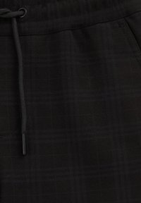 Pantaloni joggeri cu carouri negre, realizati dintr-un material moale, cu talie ajustabila cu siret, buzunare mici si variatii subtile de textura in nuante inchise.