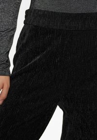 Zwarte textuurbroek met een gekreukt patroon, voorzien van een elastische tailleband. Close-up weergave toont zachte stof en gladde, glanzende accenten.
