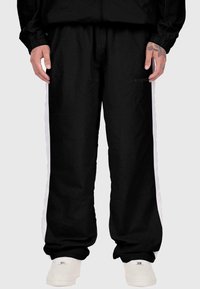 Melnas sporta bikses ar baltām sānu svītrām, izgatavotas no gludas auduma, ar elastīgu jostasvietu un uzdrukātu logo priekšpusē.