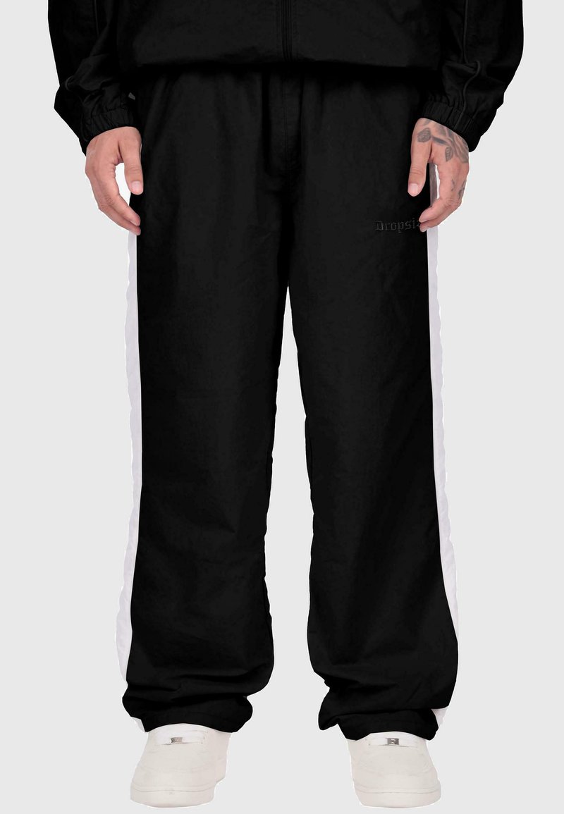 Melnas sporta bikses ar baltām sānu svītrām, izgatavotas no gludas auduma, ar elastīgu jostasvietu un uzdrukātu logo priekšpusē.