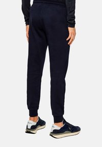 Pantaloni della tuta blu navy con vestibilità affusolata, cintura elastica e tasche laterali. Presentano una texture liscia e dettagli di cuciture sottili.