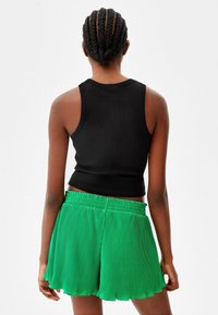 Černý proužkovaný top bez rukávů spárovaný s jasně zelenými sklady šortkami, které mají elastický pas a vlnitý lem.