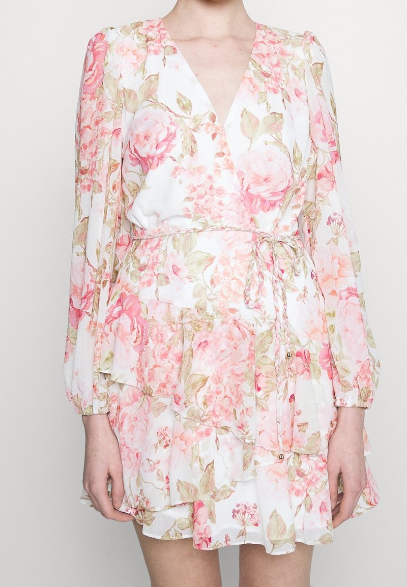 Kukkapuku vaaleassa, jossa on vaaleanpunaisia ruusuja, syvä V-mallinen kaula-aukko, pitkä puffihihna ja nyöritetty vyötärö. Aaltoileva kerroksellinen helma.