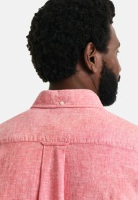 Rode gestructureerde shirt met een kraag, met een knoop aan de achterkant en een centrale plooi eronder. Stof lijkt lichtgewicht en casual te zijn.