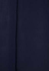 Gros plan d'un tissu bleu marine foncé avec des coutures visibles et une couture verticale au centre.