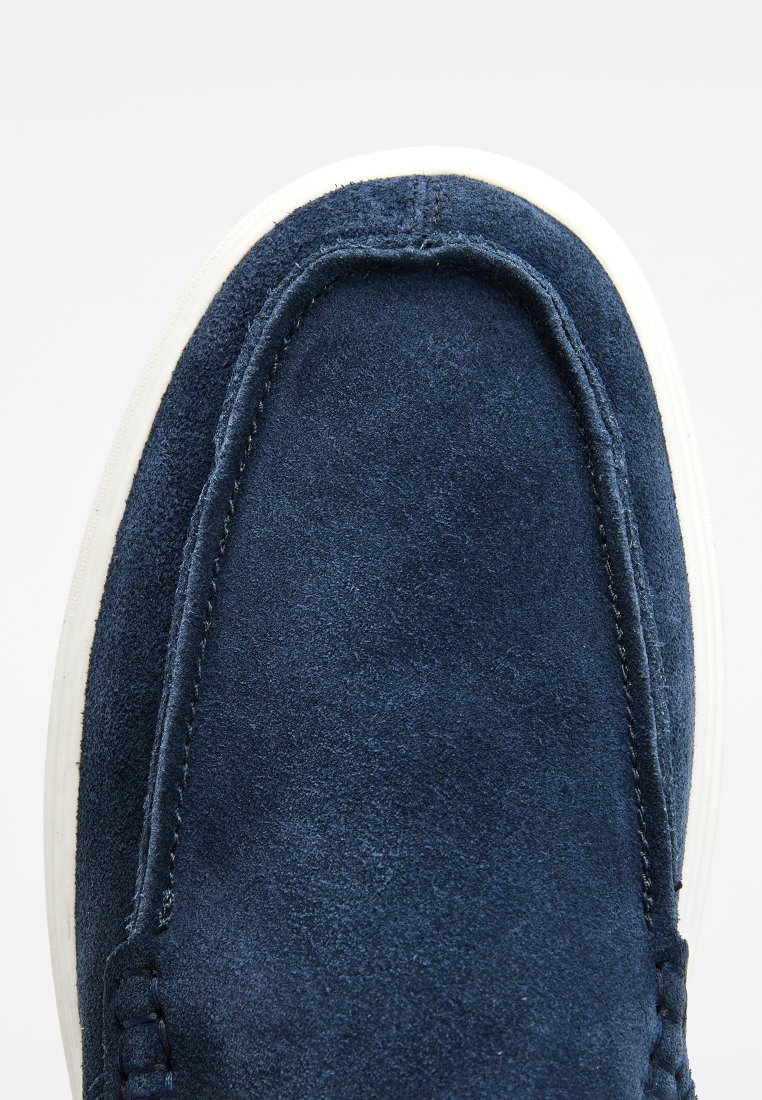 Chaussures à enfiler en daim marine avec une texture lisse, semelle extérieure blanche et couture contrastante le long de l'empeigne. Design à bout arrondi.