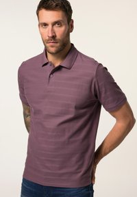 Polo shirt rayé violet à manches courtes, col et patte de boutonnage. Le tissu semble texturé et légèrement ajusté, associé à un jean.