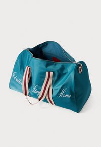 Borsa a sacca color turchese con cerniera aperta, manici a righe e scritta bianca sul lato che recita "Preferirei restare a casa."