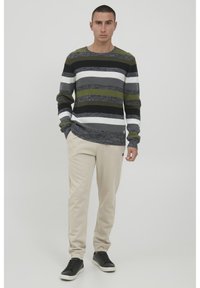 Stripet striktrøje i marineblå, grå, hvid og oliven. Parret med beige sweatpants. Sorte sneakers med grå detaljer fuldender looket.