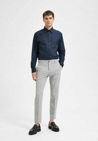 Mornarica srajca s belimi pikami, slim-fit sivi hlače in črne čevlje. Srajca ima ovratnik in gumbe, medtem ko so hlače z ravnim sprednjim delom.