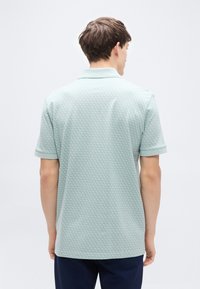 Ανοιχτό μωβ πράσινο πόλο μπλουζάκι με κοντά μανίκια, με υφασμάτινο εξαγωνικό μοτίβο και κλασικό γιακά. Εφαρμοστή γραμμή, χωρίς ορατά λογότυπα.