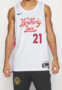 Maglia da basket bianca con dettagli rossi, testo blu con la scritta "Città dell'Amore Fraterno", numero 21 e logo NBA. Realizzata in materiale traspirante.