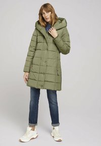 Grøn quilted puffernederdel med en stor hætte, sidelommer og lige skæring. Båret over denim og hvide sneakers med detaljering.