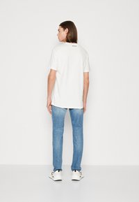 Camiseta blanca de manga corta hecha de algodón, con un cuello redondeado y un pequeño logo impreso en la parte posterior, combinada con jeans de color azul claro.