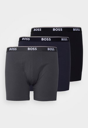 Boxershorts in Grau, Dunkelblau und Schwarz. Weiches Baumwollmaterial mit einem dehnbaren Bund, der das "BOSS"-Logo in Weiß trägt. Jede Variante ist mittellang.