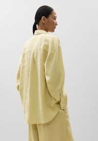 Camicia di lino gialla chiara con vestibilità rilassata, maniche lunghe e polsini con bottone. Presenta una piega sul retro per una maggiore libertà di movimento.