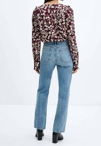 Blouse à motifs floraux en bordeaux profond et crème ; jean taille haute bleu clair ; bottines à talons noires ; vue arrière mettant en avant les détails du vêtement.