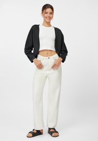 Svart kort jacka, vit åtsittande topp, vida krämfärgade byxor och svarta sandaler med korkklack. Slätt tyg och avslappnad silhuett.