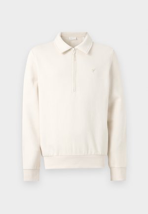 Pulover dolgi rokavi v krem barvi s četrtinskim zadrgo, ovratnikom, rebrastimi manšetami in majhnim vezenim logotipom na levi strani prsi.