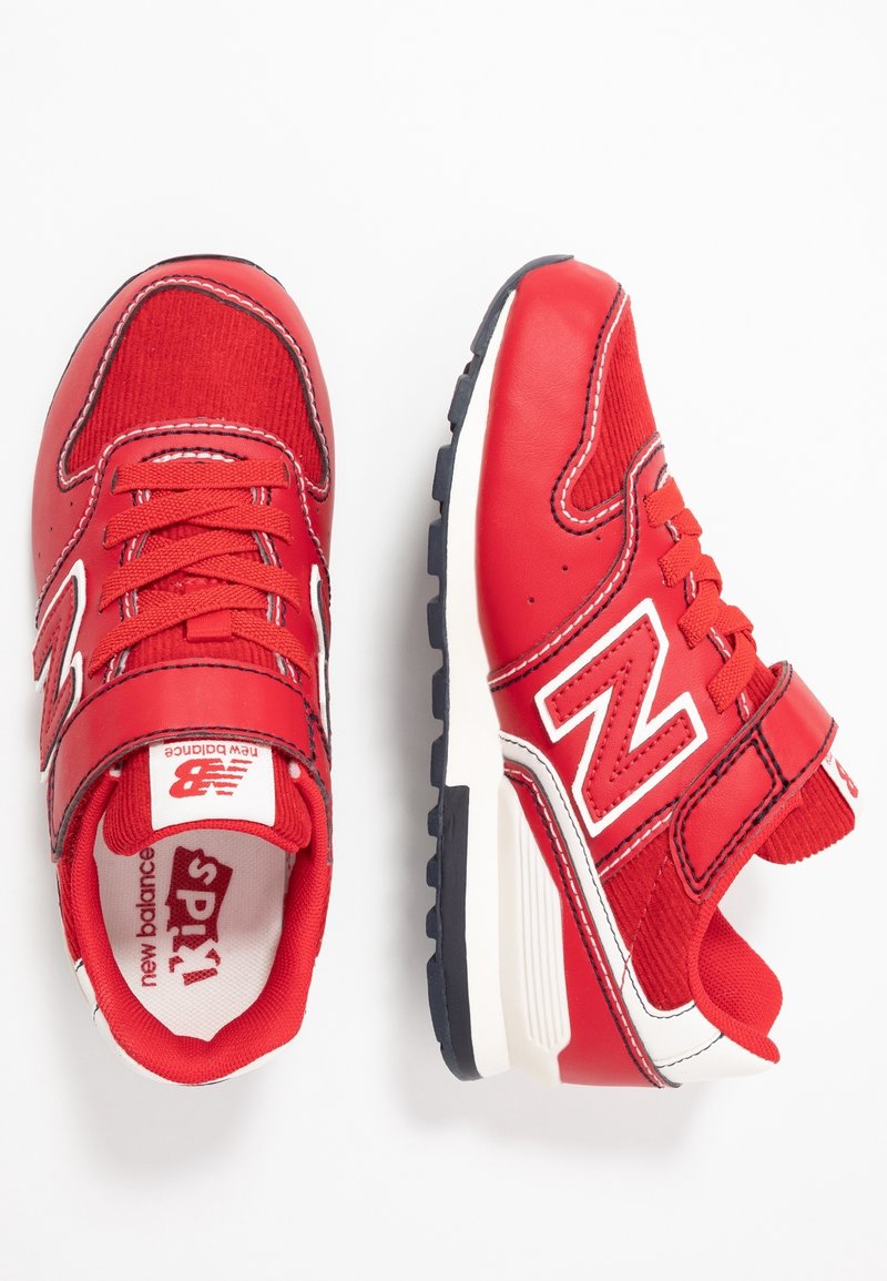 Une paire de baskets rouges pour enfants de New Balance avec des accents blancs, des bandes Velcro et des semelles noires, présentées de vue supérieure et latérale sur fond blanc.