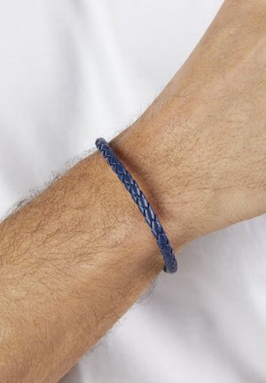 Marineblaues geflochtenes Lederarmband an einem Handgelenk, mit einer glatten Textur und abgerundeter Form, die eng am Handgelenk anliegt.