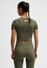 Olivengroene geribbelde cropped top met korte mouwen, voorzien van een label aan de achterkant. Gecombineerd met bijpassende high-waisted leggings. Glad oppervlak.