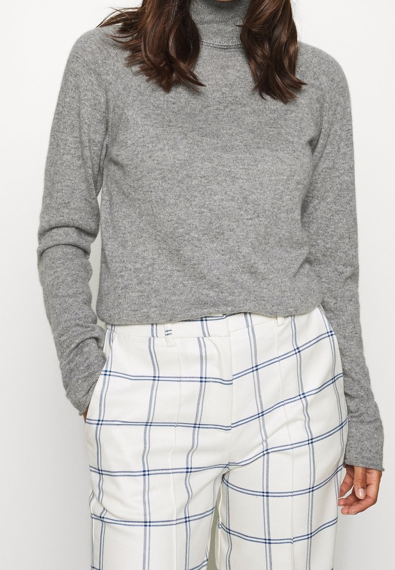 Grauer Rollkragenpullover mit langen Ärmeln, kombiniert mit weißen Karo-Hosen mit blauen Linien, die einen strukturierten Stoff betonen.