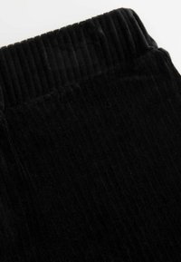 Czarny materiał kordurowy o żebrowanej teksturze. Obraz koncentruje się na górnej części, która ma szeroki, elastyczny pas.