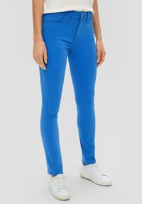 Strakke blauwe spijkerbroek van denim met een gladde textuur, vijf-pocket ontwerp en subtiele stiksels. Gecombineerd met witte sneakers.