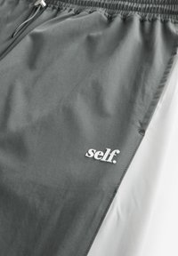 Gray and white casual pants with elastic waistband and drawstring, featuring the word "self." printed in white on the gray section.