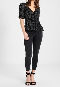 Svart blus med prickar, v-ringad hals, kort puffärmar och peplumsläpp, ihop med svarta skinny jeans och svarta snörsandaler.