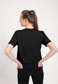 T-shirt in cotone nero con maniche corte, collo rotondo e una vestibilità rilassata, abbinato a jeans neri. Il tessuto appare liscio e privo di fantasie.