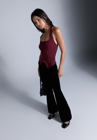 Burgundské halter top s přiléhavým korzetem a zapínáním na knoflíky, v kombinaci s černými sametovými zvonovými kalhotami a lesklými černými botami.