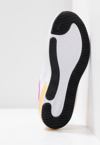 Shoe features a white upper with pink accents, textured fabric, and black rubber sole with traction patterns. Yellow midsole detail included.