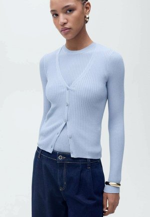 Light blue ribbed cardigan with a V-neck and button closure. Long sleeves with a fitted silhouette. Paired with high-waisted dark denim.