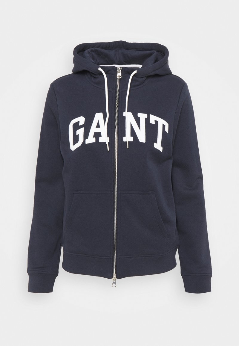 Felpa con zip navy in tessuto misto cotone. Presenta una grande stampa bianca "GANT" sul davanti, cappuccio con cordino e tasche frontali.