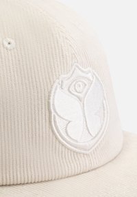 White corduroy cap with a textured surface, featuring a prominent white embroidered logo resembling a butterfly and a rose.