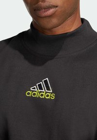 Svart sweatshirt med høy hals, som har en hvit og neongrønn brodert Adidas-logo og ribbet tekstur nær kragen.