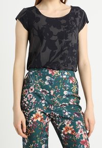 Camisa negra de manga corta con estampado floral, combinada con pantalones verdes que presentan coloridos patrones de flores. Tejido suave, diseño de ajuste relajado.