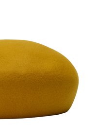Okrąła, musztardowo-żółta poduszka z filcu o gładkiej, miękkiej fakturze na białym tle.