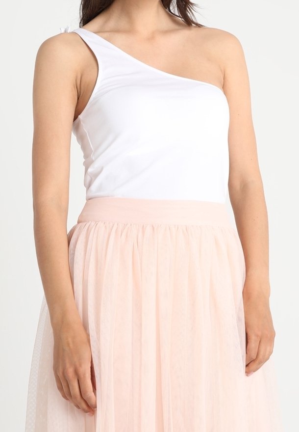 Witte one-shoulder top van rekbaar materiaal, gecombineerd met een zachtroze tule rok met een gerimpelde taille en gelaagde structuur.