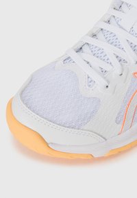 Hvite sportsko med mesh-overdel, syntetiske detaljer og oransol såle. Har en avrundet tå og standard snøring.