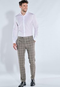 Hellblaues Hemd kombiniert mit braunen, karierten Hosen. Die Hosen haben eine glatte Textur, einen Knopfverschluss und ein schlankes Design. Schwarze Schuhe komplettieren das Outfit.