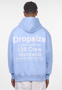 Hellblaue Kapuzenjacke mit einer Kordelzugkapuze, auf der Rückseite mit großem weißen Text: "Dropsize Limited Collection 030 Crew Worldwide."