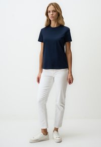 T-shirt in cotone blu navy con maniche corte e colletto rotondo, abbinato a jeans bianchi a gamba dritta e sneakers bianche. Design semplice.