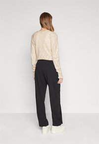 Beige knit sweater with diamond pattern, black wide-leg pants, and white sneakers, viewed from the back, highlighting texture and fit.